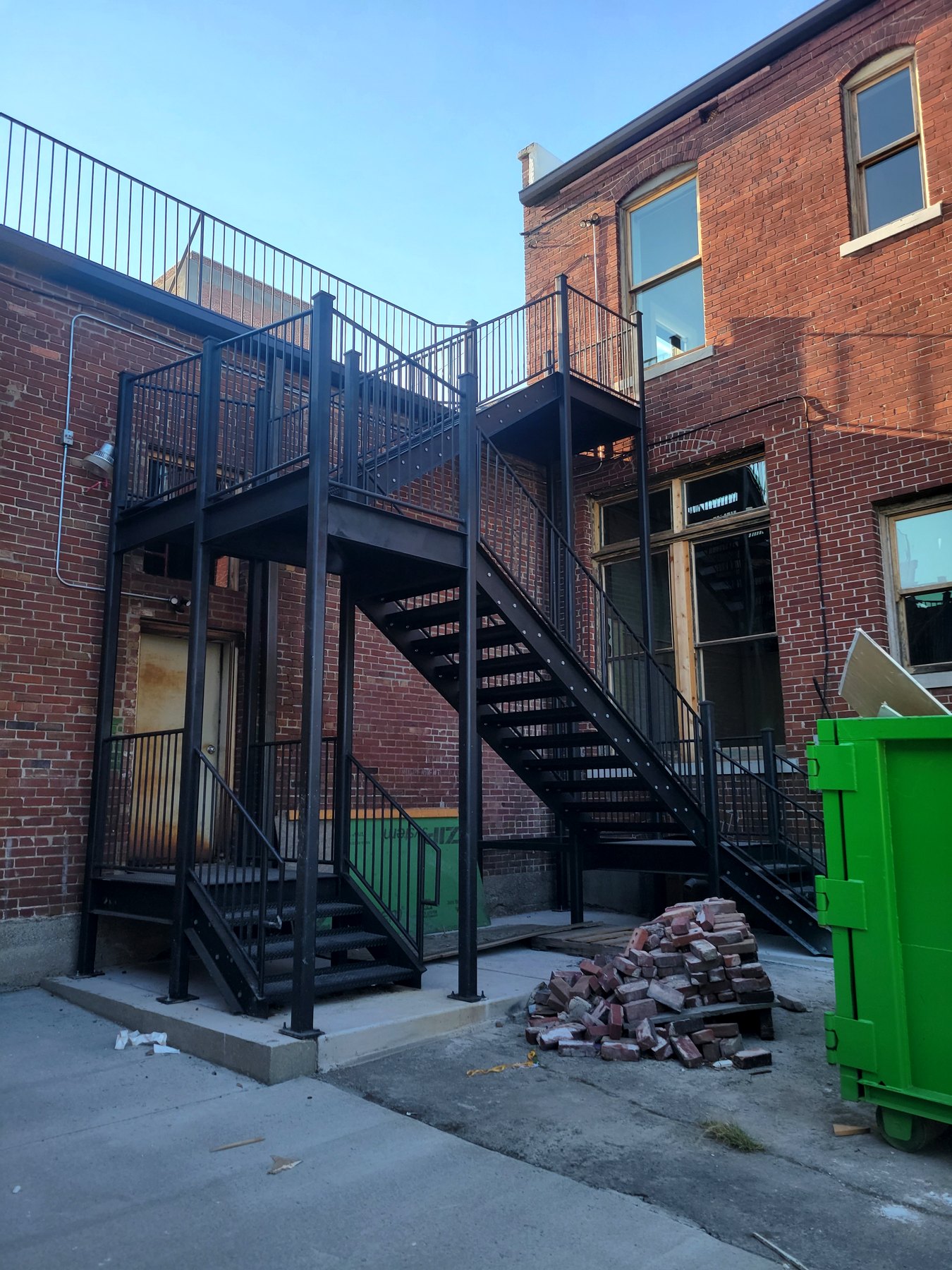 Ground-level view of a black steel stair and platform installation beside a brick building