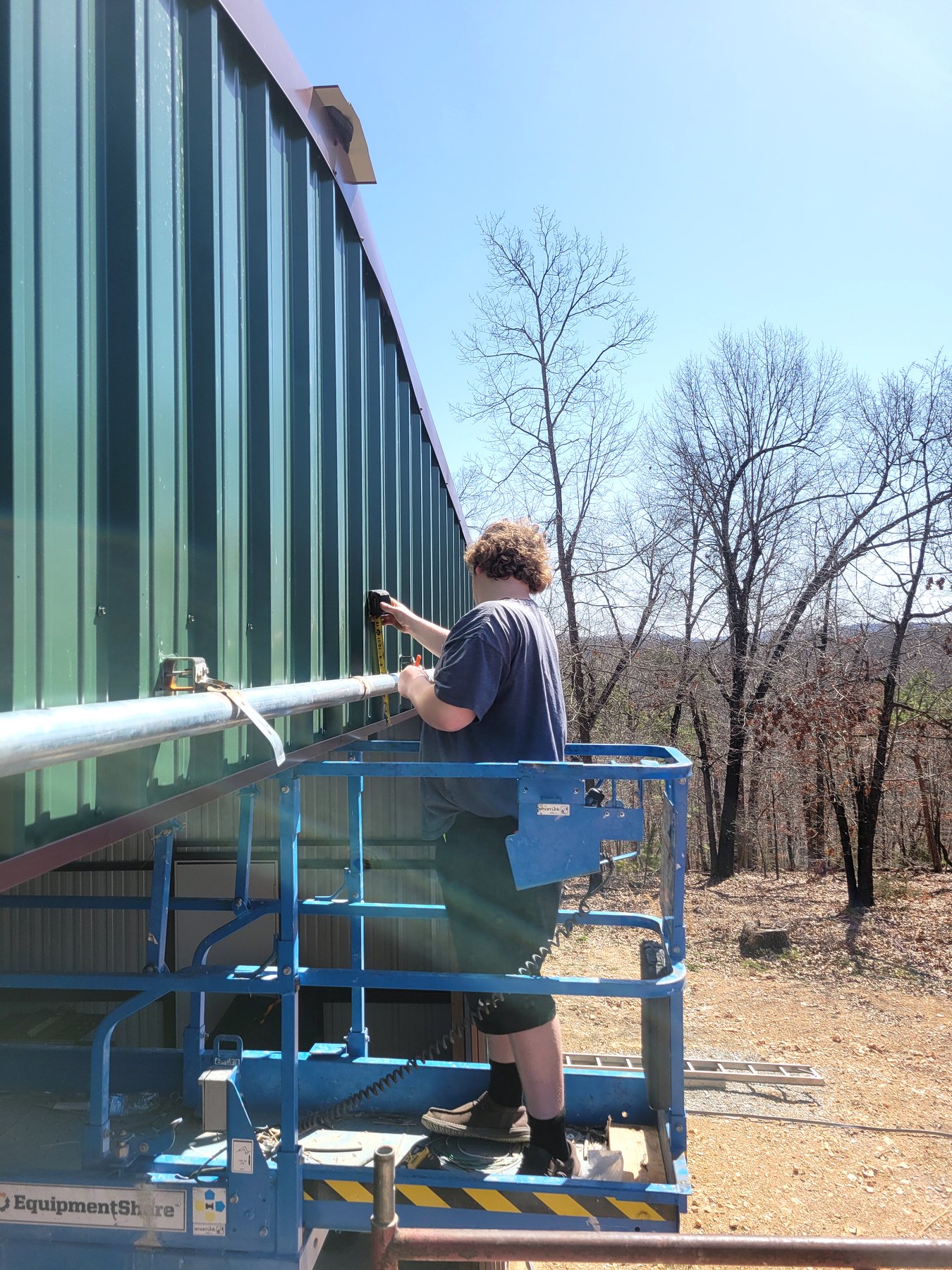 Worker on lift installing metal siding on a commercial building